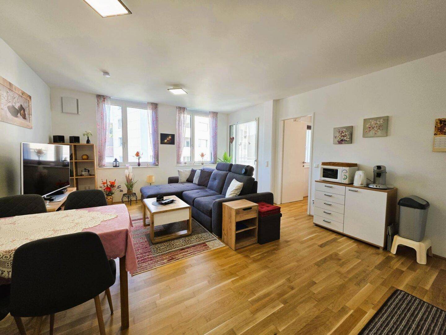 Geräumiger Wohn- und Essbereich mit Holzboden, bequemer Couch und mehreren Fenstern.