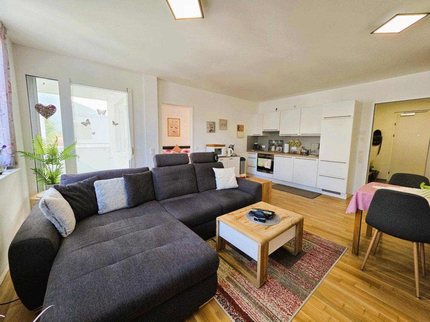 Offener Wohnbereich mit großem Ecksofa, Holzboden und Zugang zum Balkon.