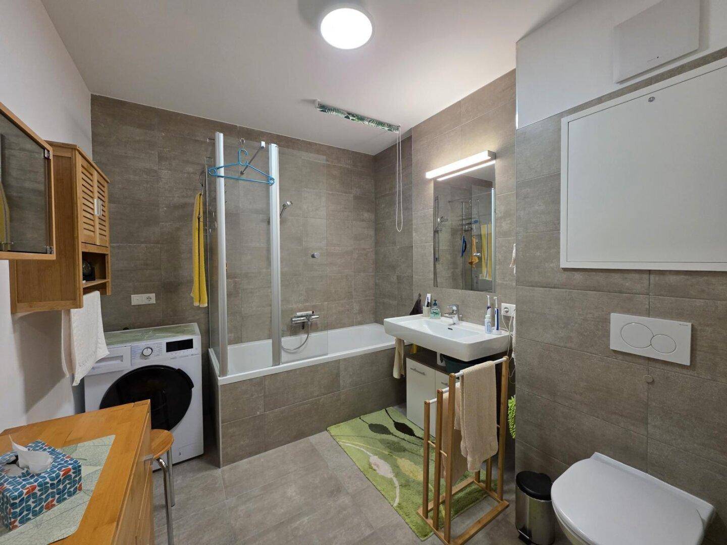 Modernes Badezimmer mit Badewanne, Dusche, WC, Waschbecken und Waschmaschine.
