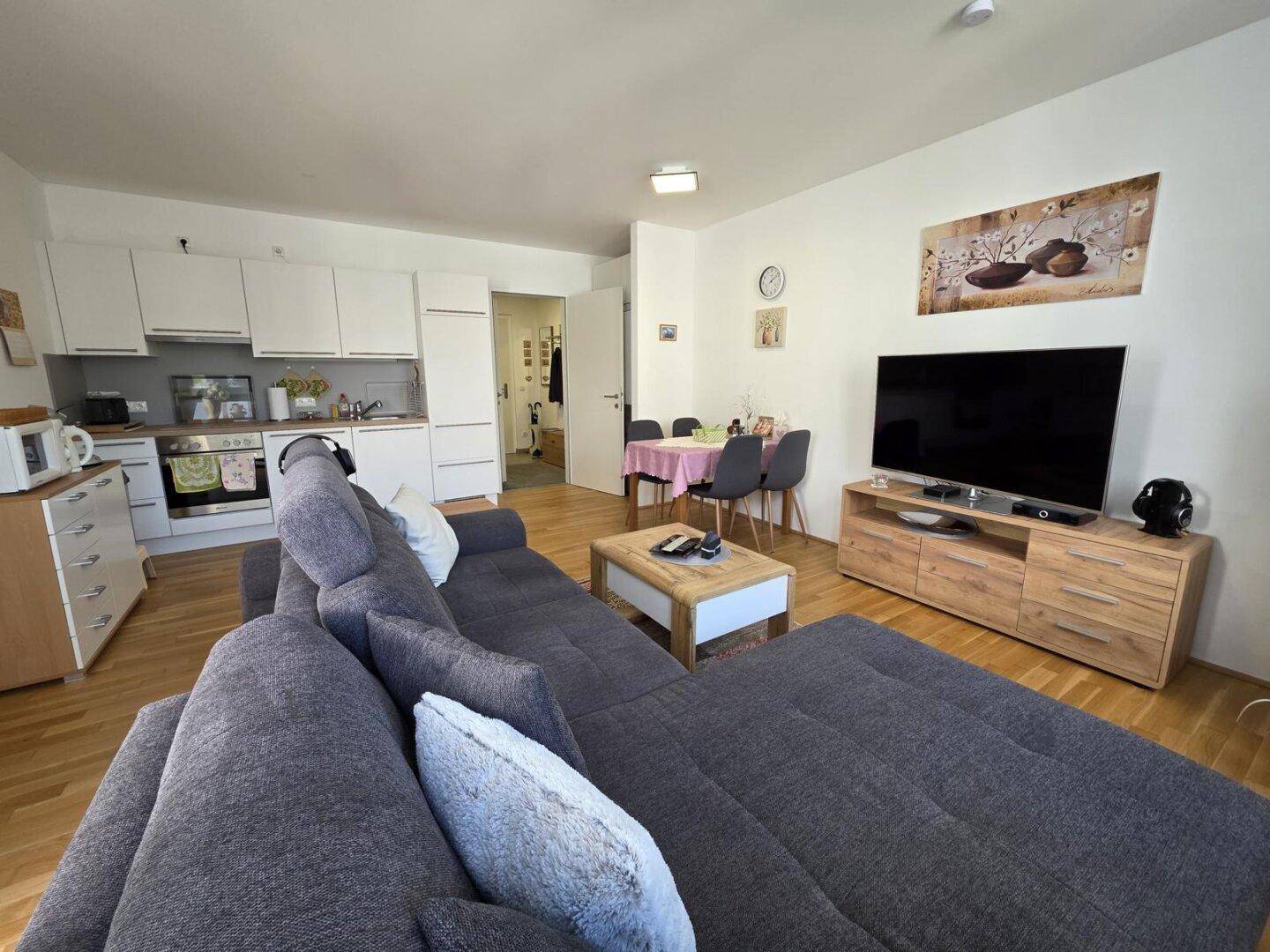 Heller Wohnbereich mit integrierter Küche, großem Sofa und Fernseher.