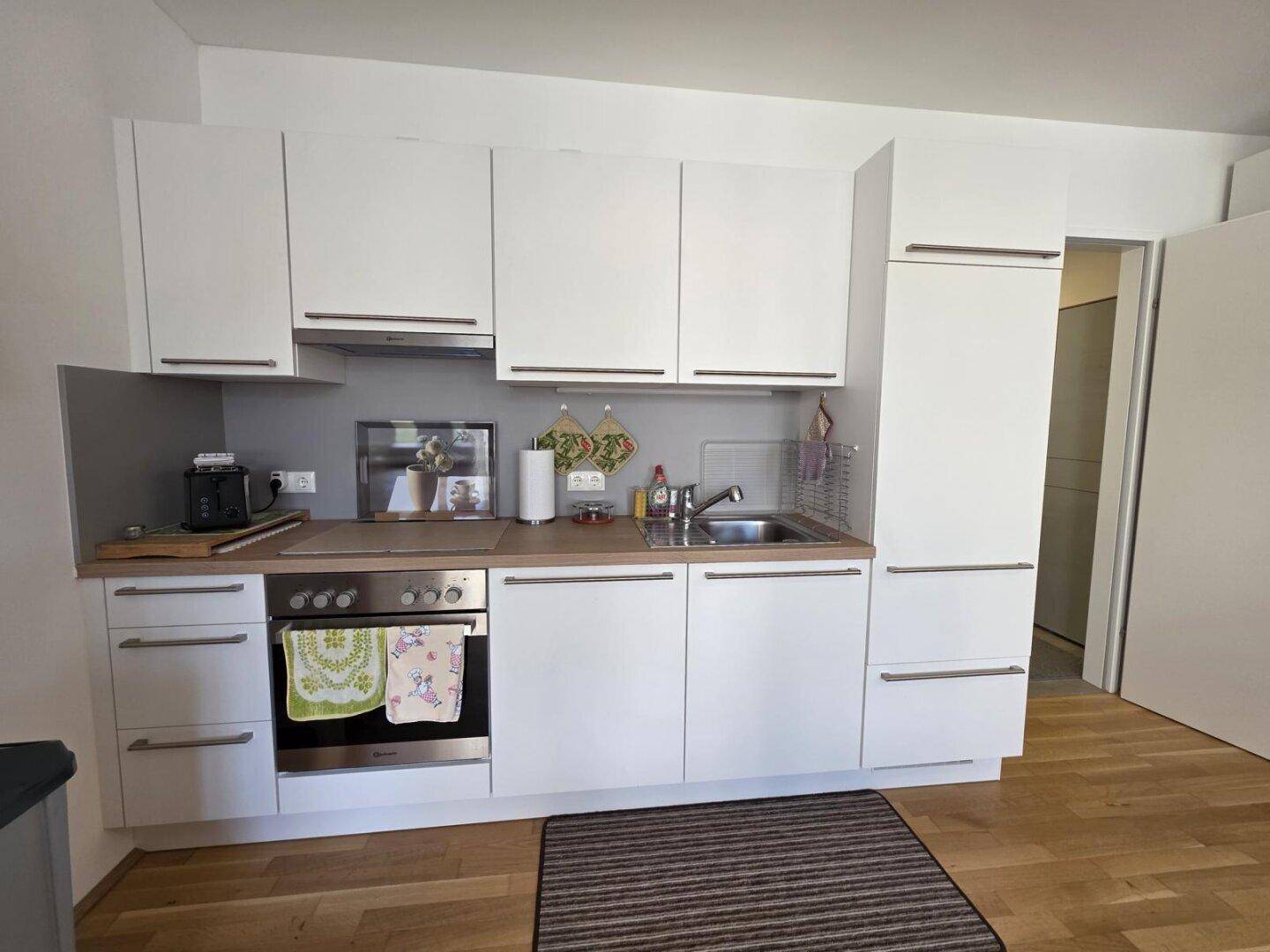 Moderne Einbauküche mit weißen Schränken, Holz-Arbeitsplatte und integriertem Backofen.