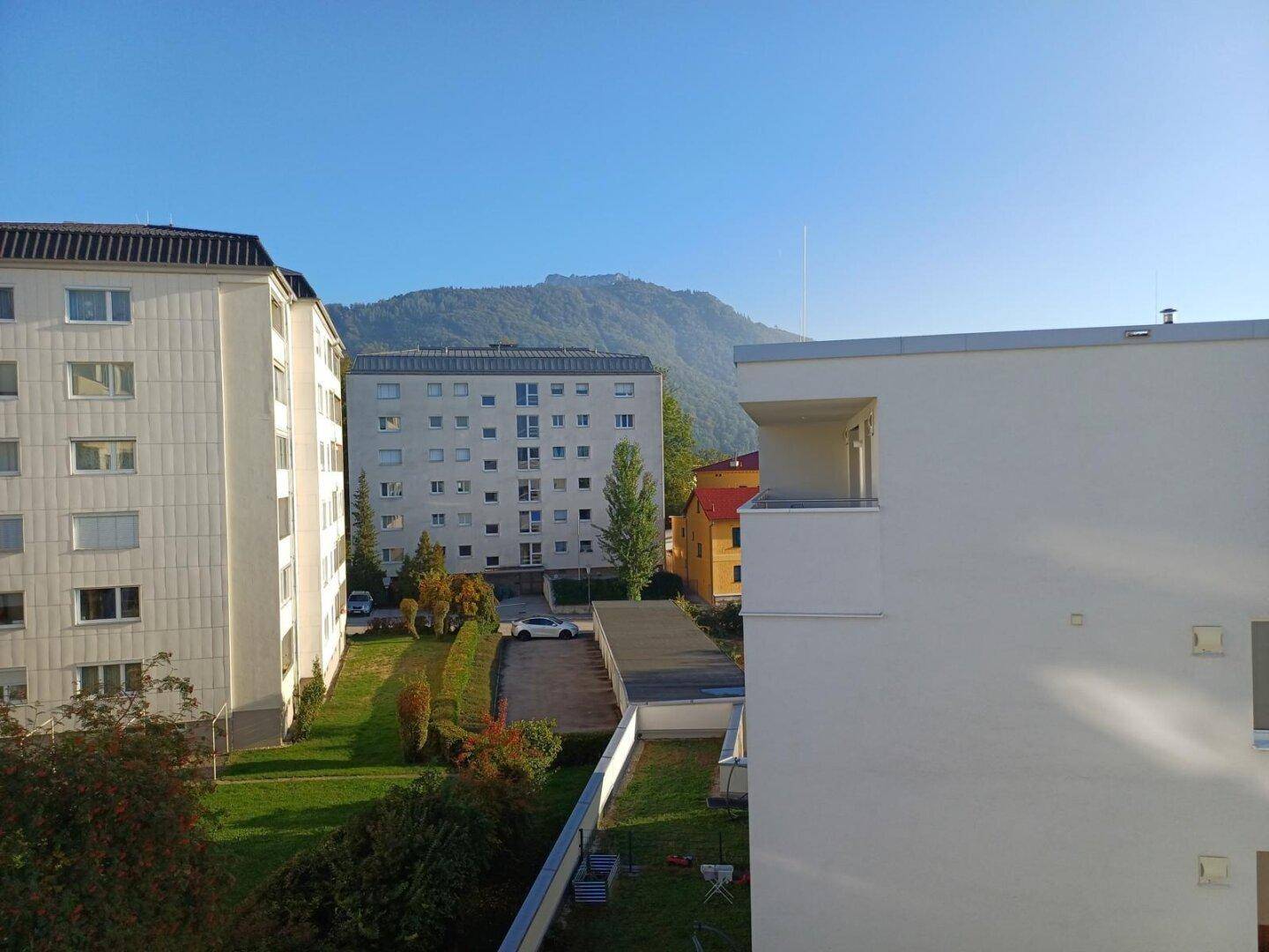 Weitblick über Wohngebäude, Grünflächen und die umliegende Berglandschaft.