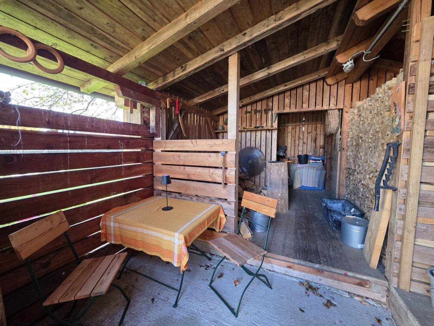 Rustikaler Holzschuppen mit kleinem Tisch und Stühlen, ideal als Werkstatt oder Abstellraum.