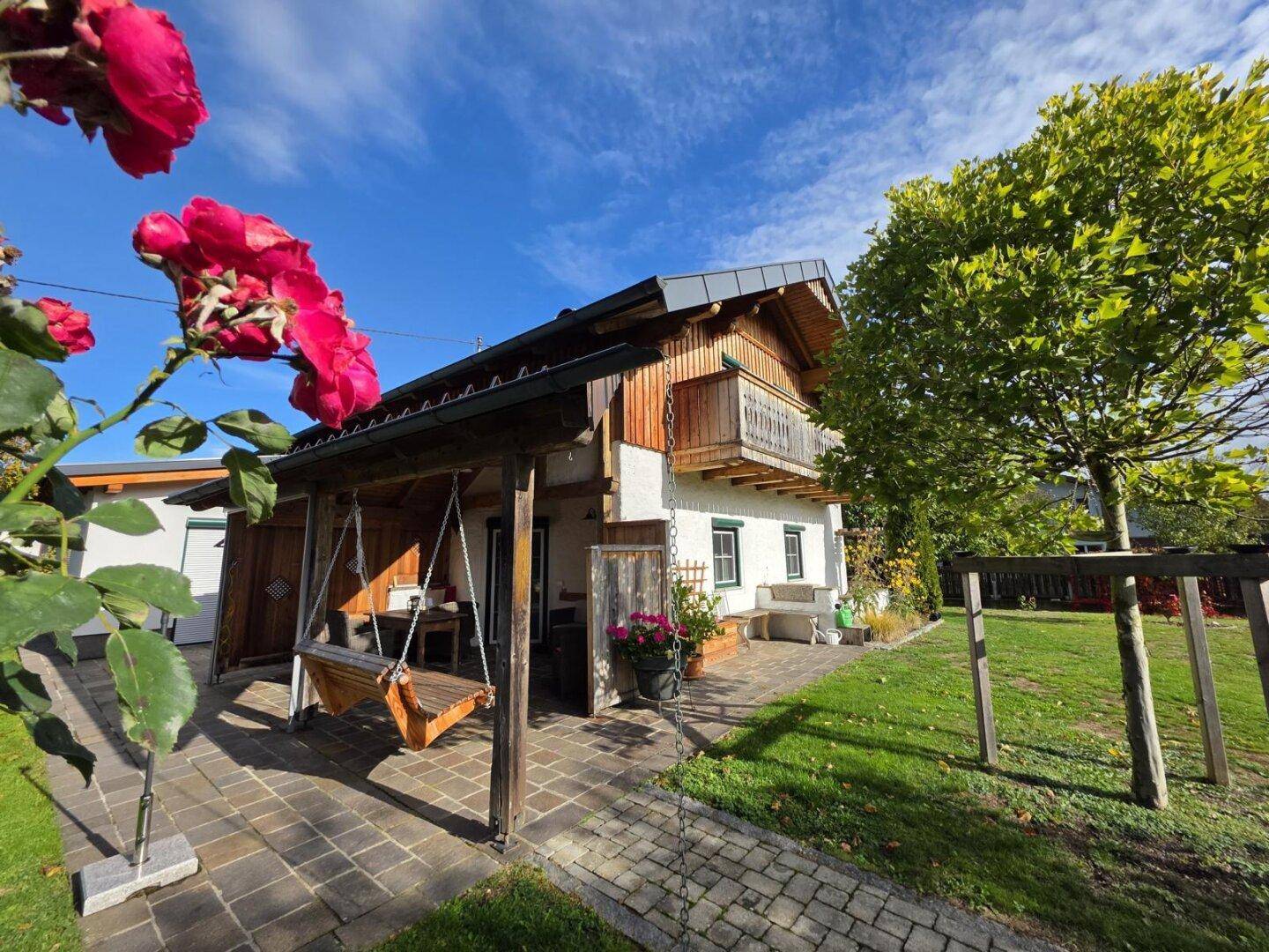 Gemütliche Terrasse mit Holzschaukel und Zugang zum Garten, umgeben von grüner Natur.