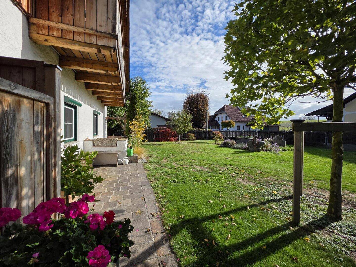 Weitläufiger grüner Garten neben dem Haus mit gepflastertem Weg und blühenden Pflanzen.