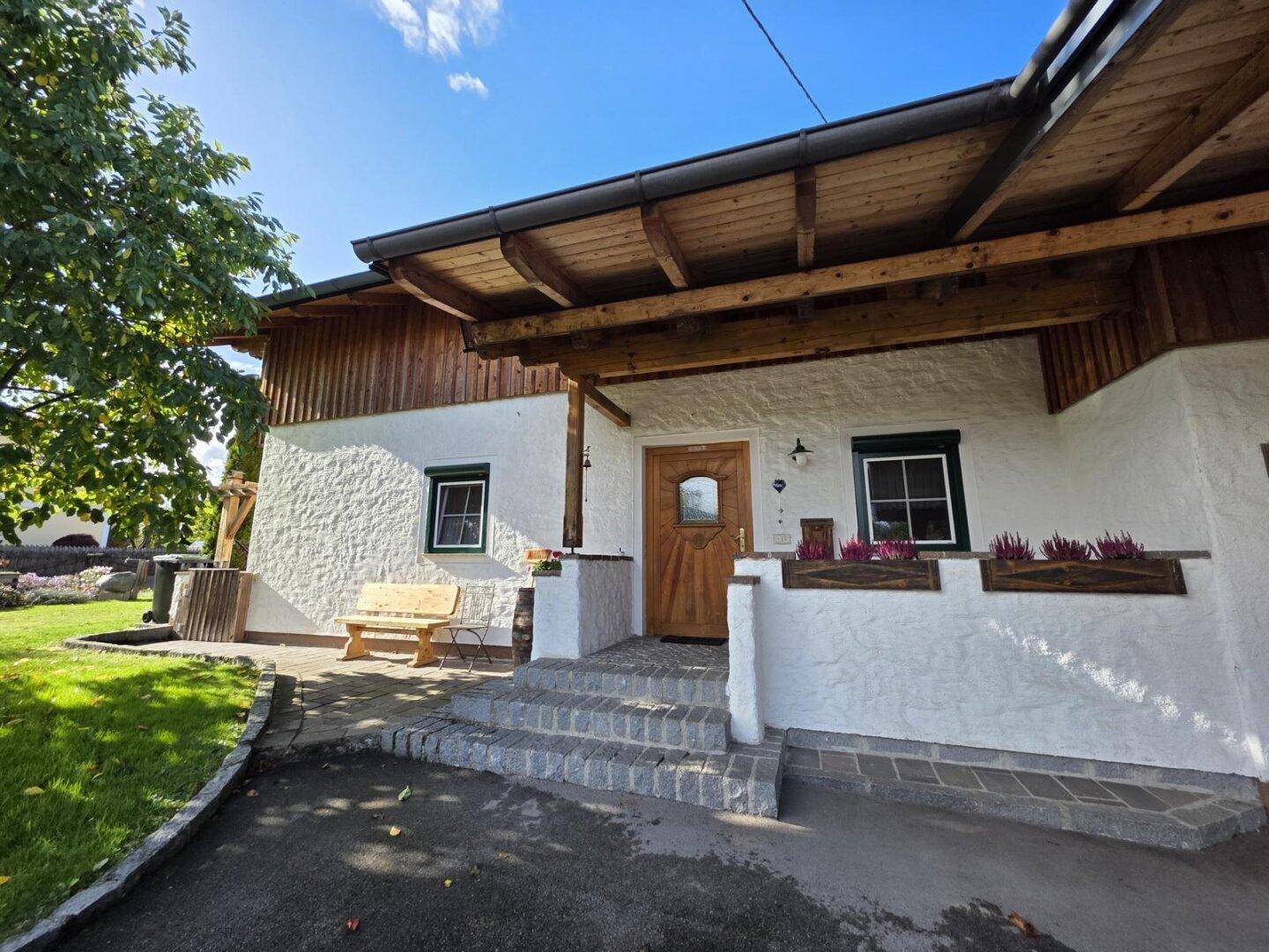 Eingangsbereich des Hauses mit Holztür, kleinen Fenstern und einer gepflasterten Treppe.