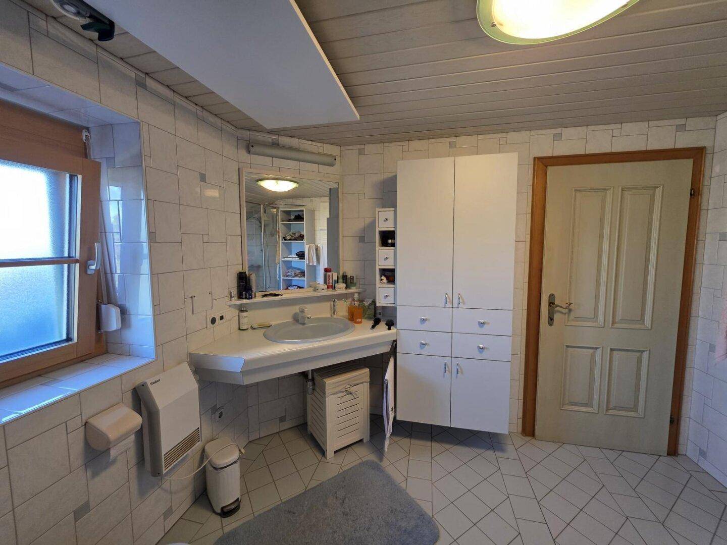 Funktionales Badezimmer mit Waschbecken, Spiegelschrank und weißem Stauraumschrank.