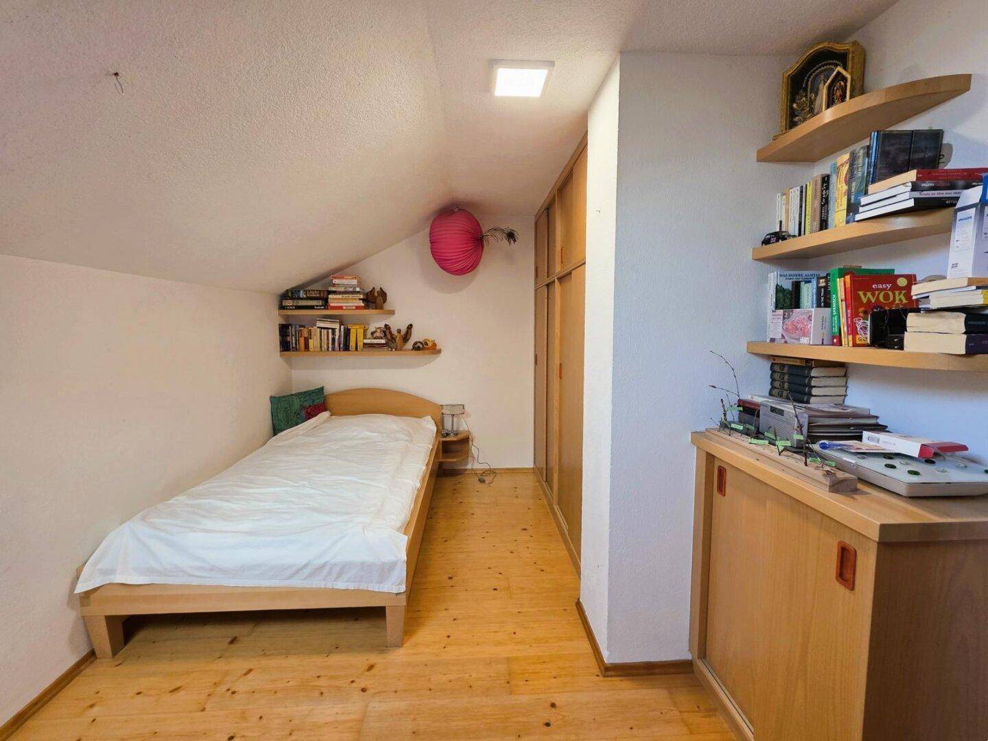 Gemütliches Schlafzimmer im Dachgeschoss mit Einzelbett, Holzschrank und Regalen.