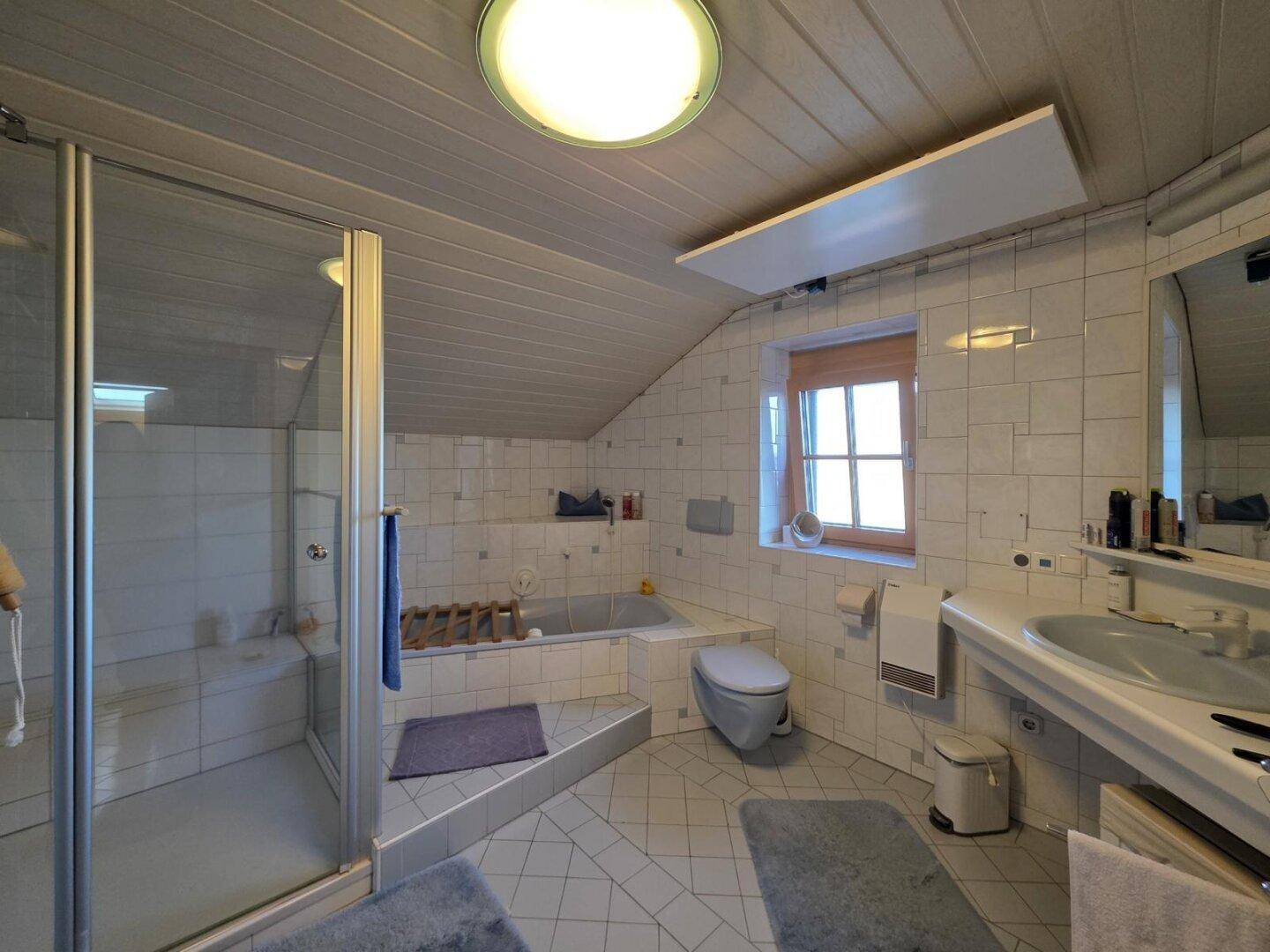 Gefliestes Badezimmer im Dachgeschoss mit Dusche, Badewanne und Fenster.