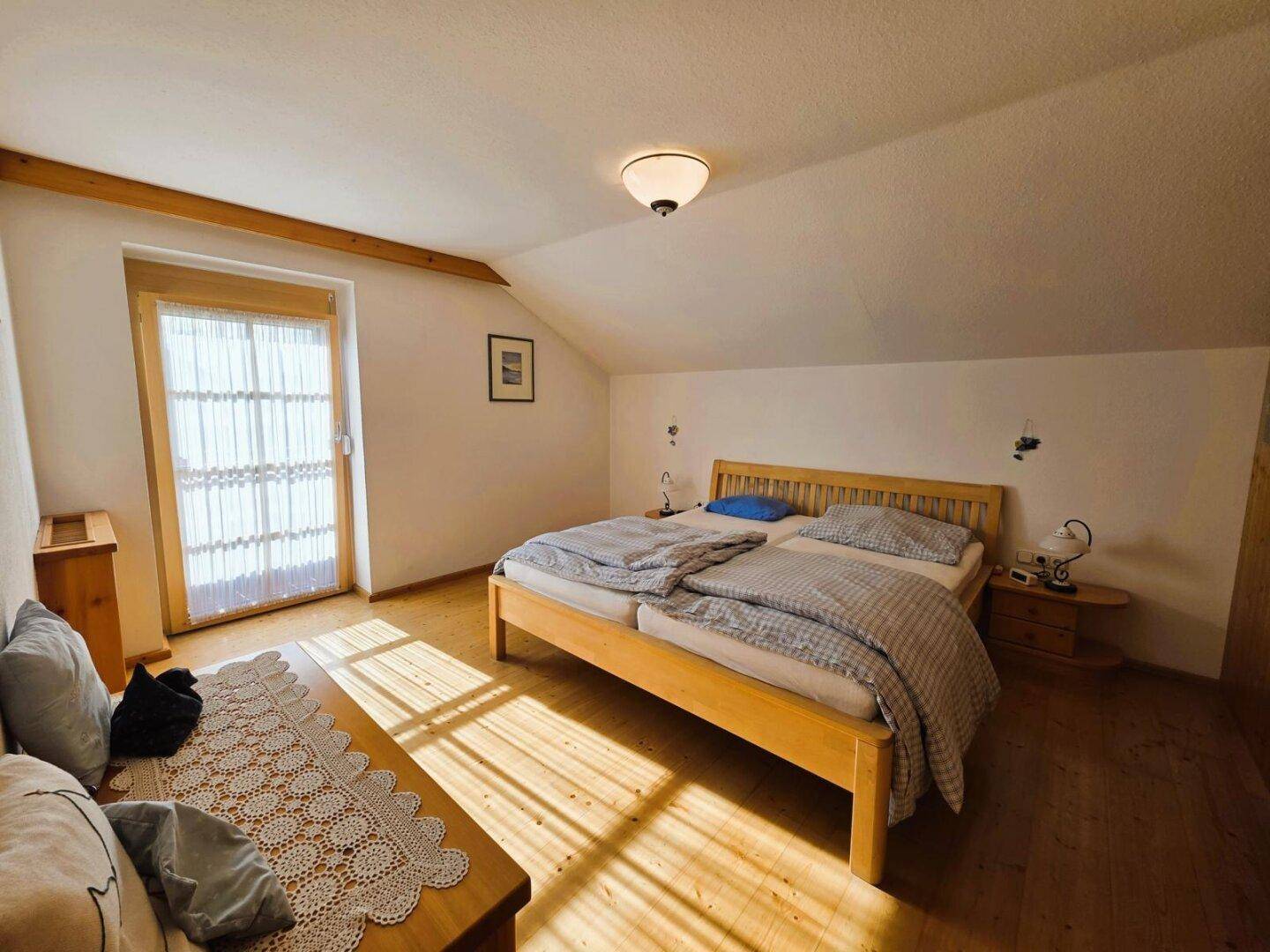 Helles Schlafzimmer im Dachgeschoss mit Holzboden und Zugang zu einem Balkon.