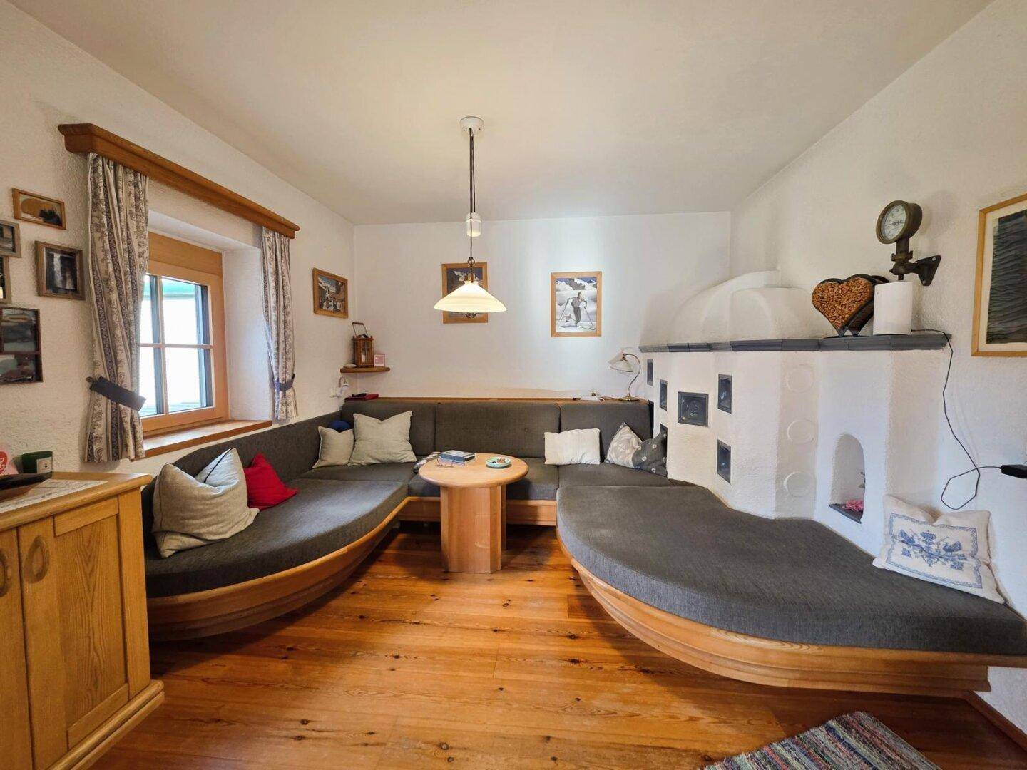 Traditionelles Wohnzimmer mit Holzboden, Kachelofen und bequemen Sitzbänken.