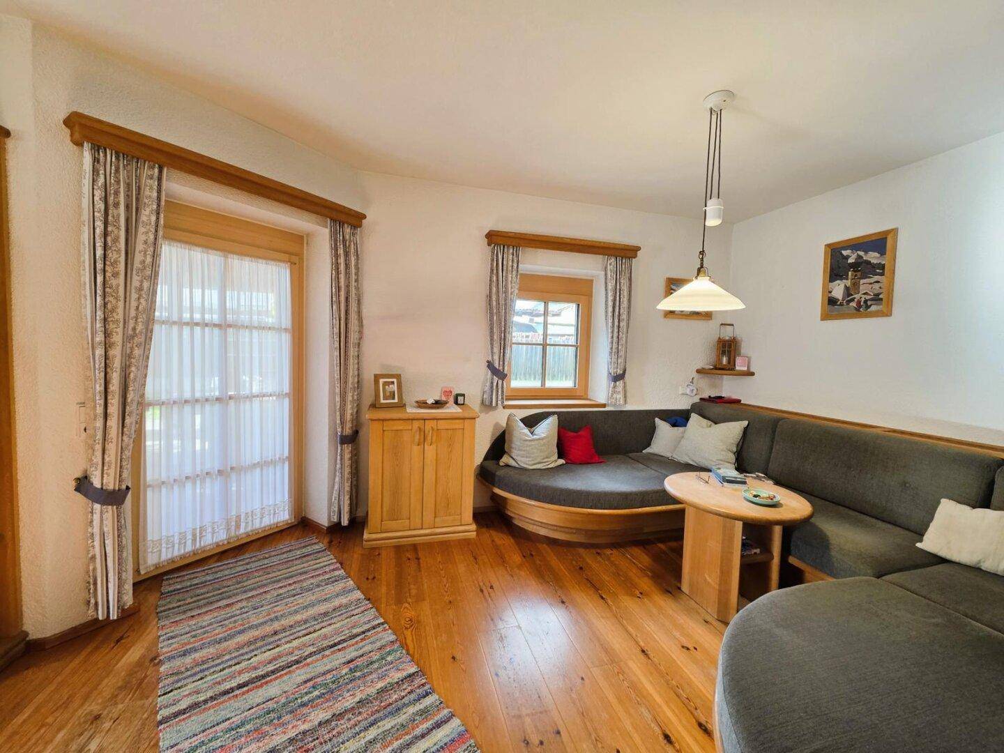 Helles Wohnzimmer mit Holzboden und Zugang zu einem Außenbereich, eingerichtet im Landhausstil.