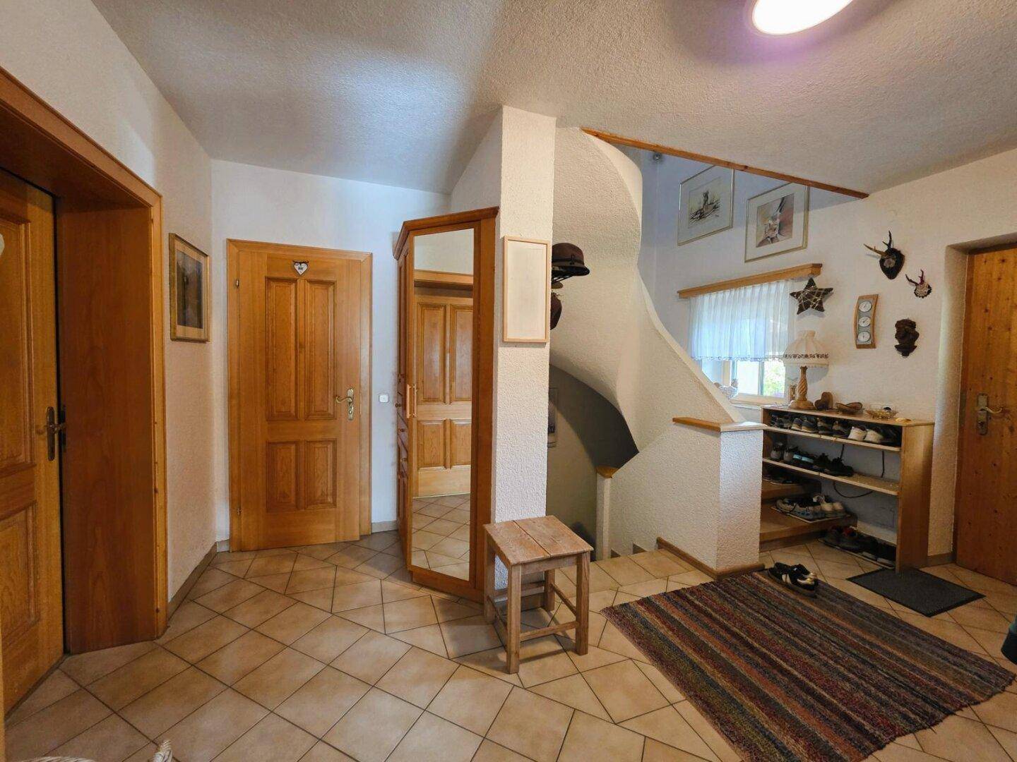 Geräumiger Flur mit Fliesenboden, Holzmöbeln und Treppenaufgang zum Obergeschoss.