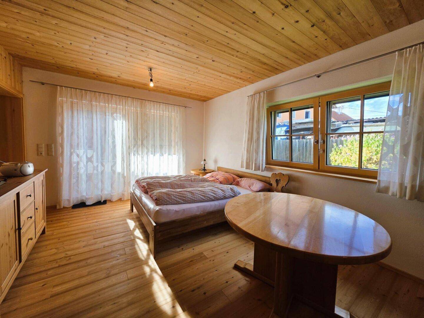 Geräumiges Schlafzimmer mit Holzboden, Holzdecke und viel Tageslicht durch große Fenster.