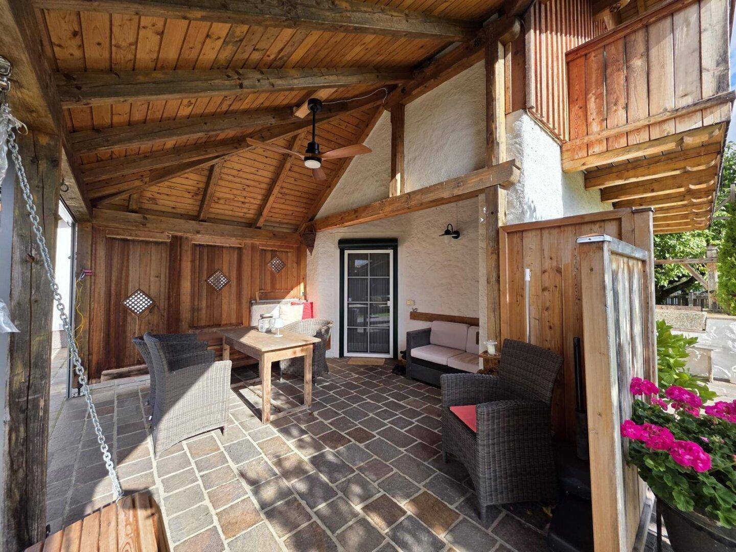 Geräumige überdachte Terrasse mit Holzdecke, Deckenventilator und gemütlichen Sitzmöbeln.