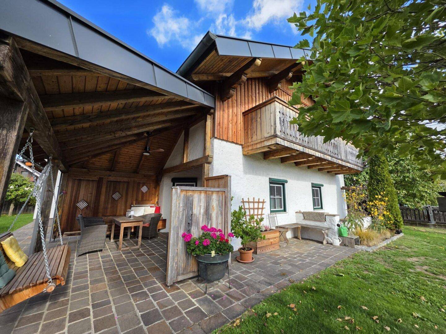 Überdachte Terrasse mit Holzschaukel und Sitzgelegenheiten, angrenzend an den Gartenbereich.
