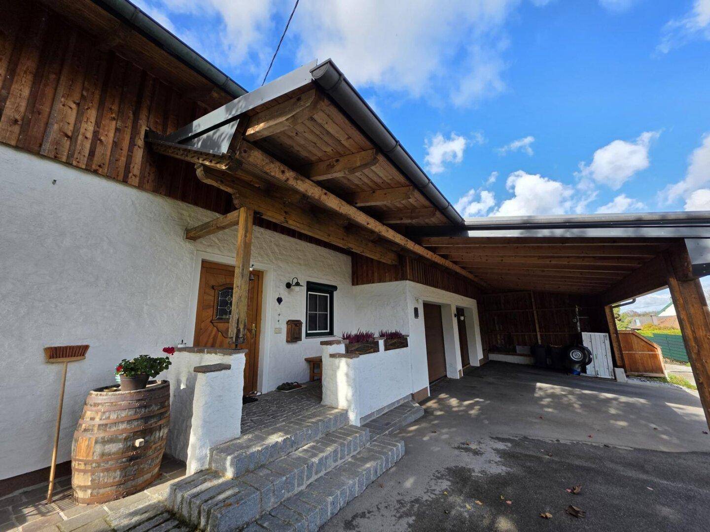 Eingangsbereich des Hauses mit gepflasterter Treppe und großem Carport aus Holz.