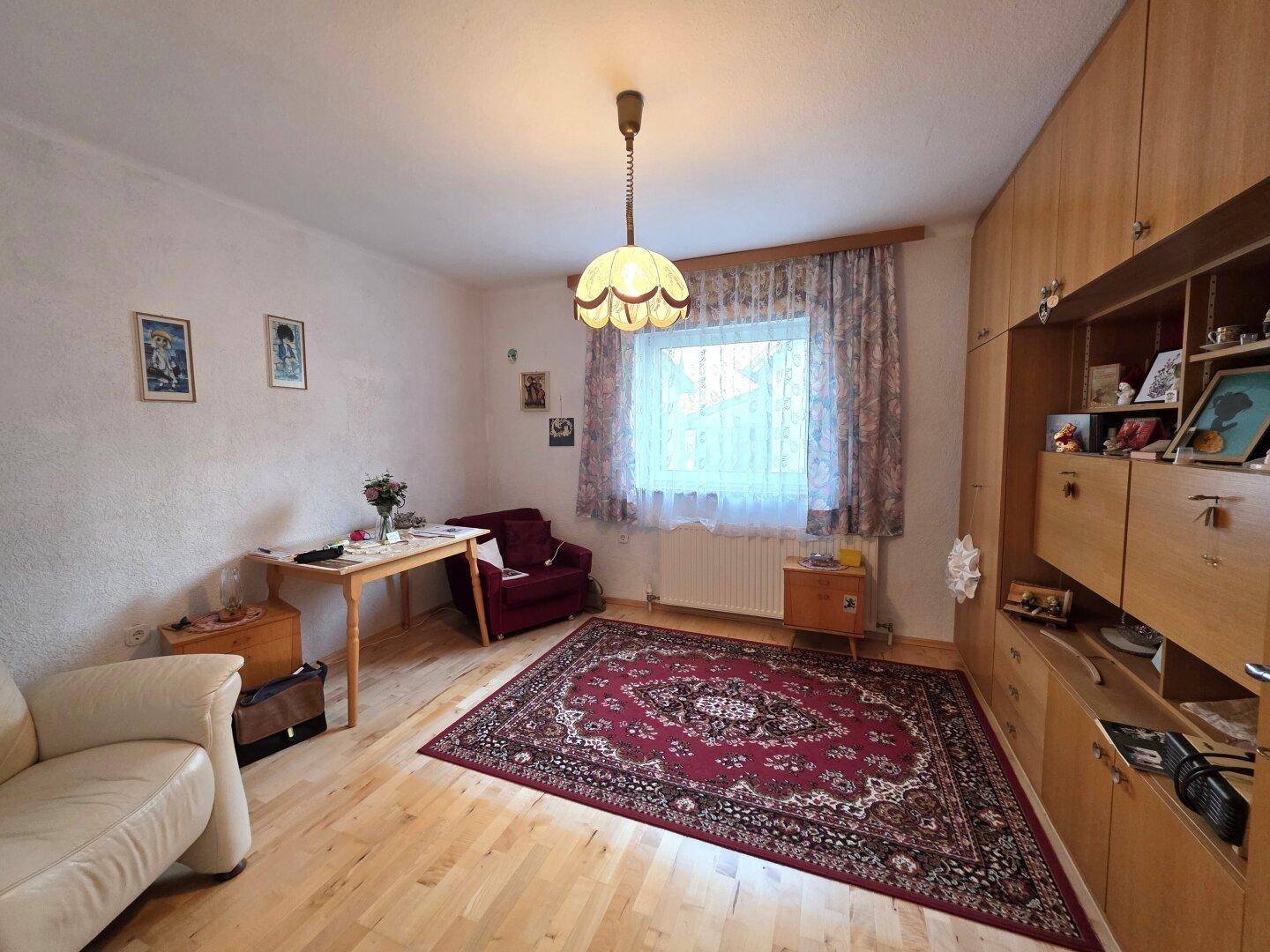 Helles Wohnzimmer mit Holzparkett, großem Schrank und traditionellem Teppich.