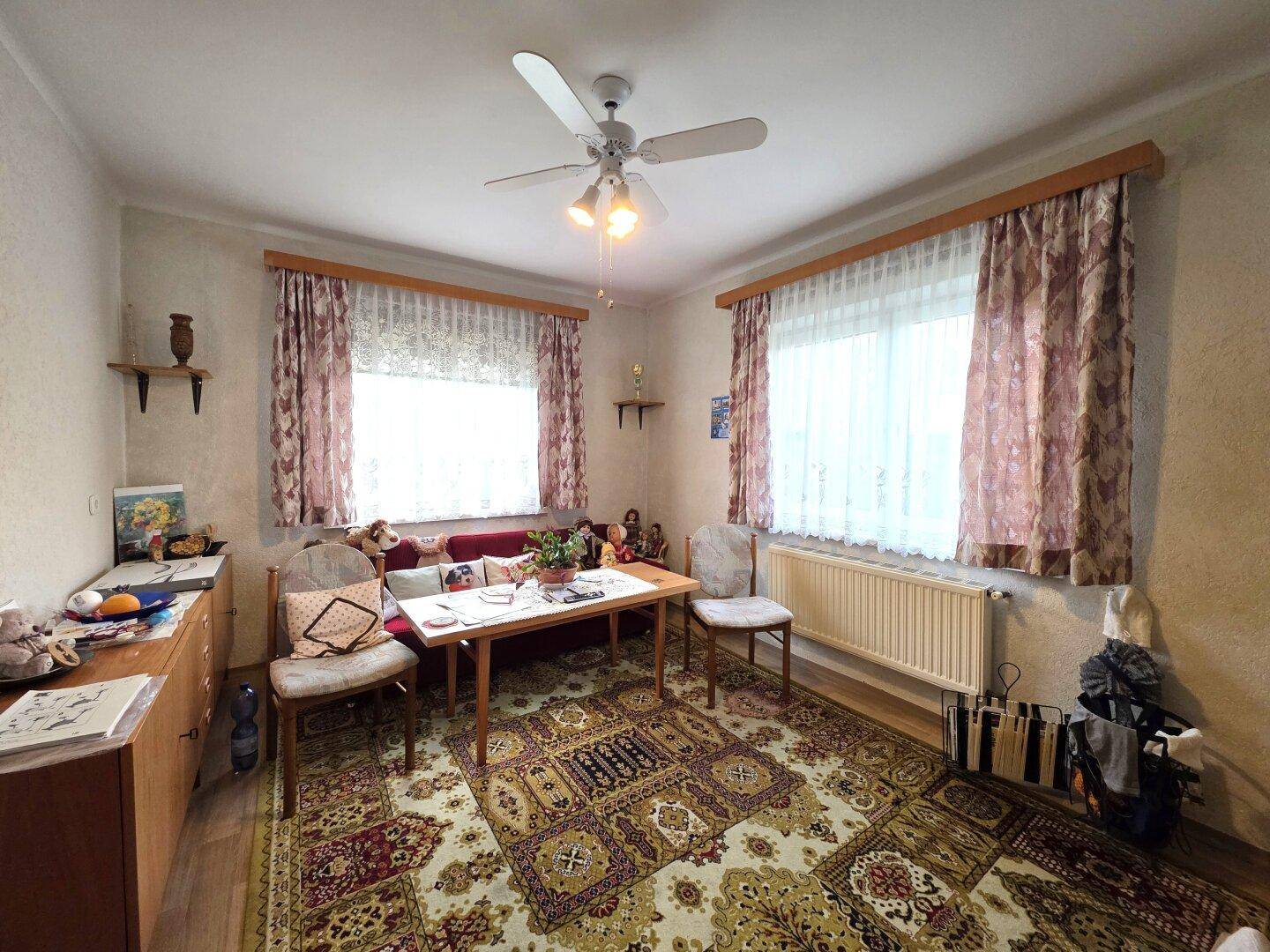 Schlafzimmer mit zwei Fenstern, Deckenventilator und traditionellem Teppichboden.