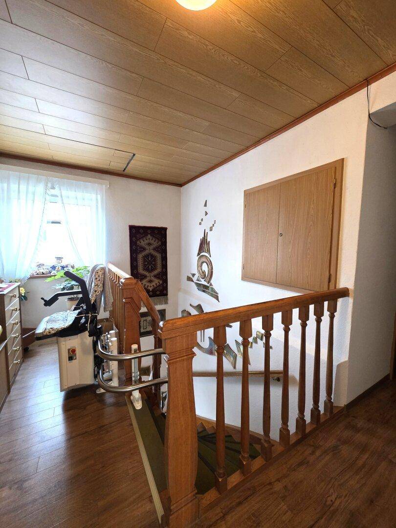 Flur mit Holztreppe, Treppenlift und Holzpaneeldecke.