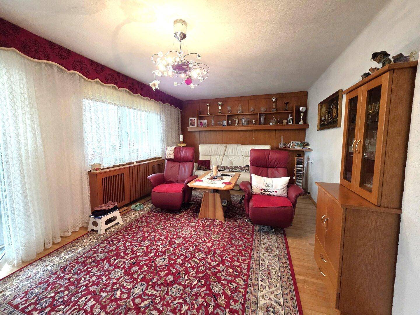 Gemütliches Wohnzimmer im traditionellen Stil mit rotem Teppich, Holzmöbeln und großen Fenstern.