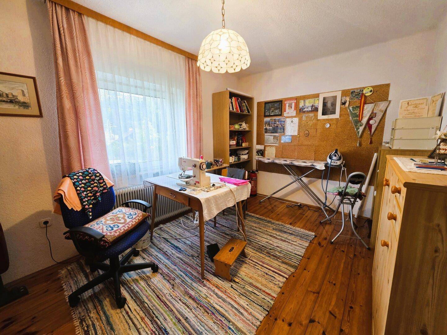 Arbeitszimmer mit Nähmaschine, Holzparkett und großem Fenster.