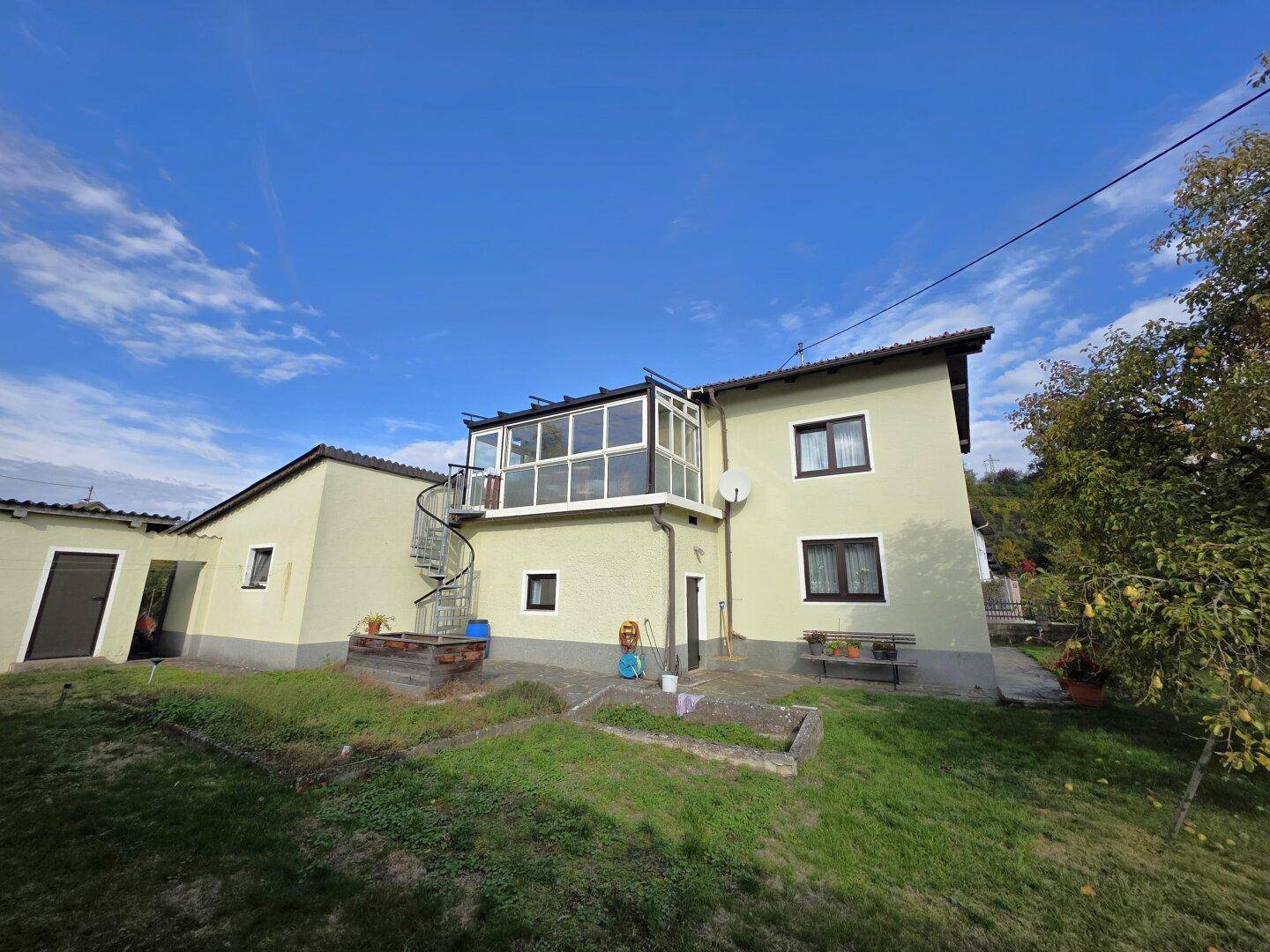 Rückansicht des Hauses mit Wintergarten, Außentreppe und weitläufigem Gartenbereich.