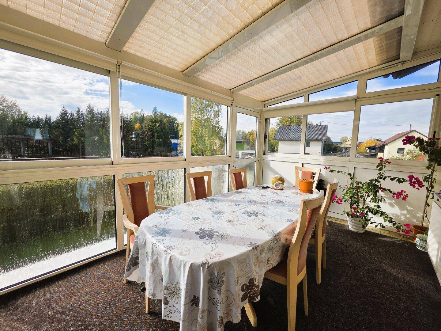Heller Wintergarten mit Esstisch, großen Fenstern und Blick ins Grüne.