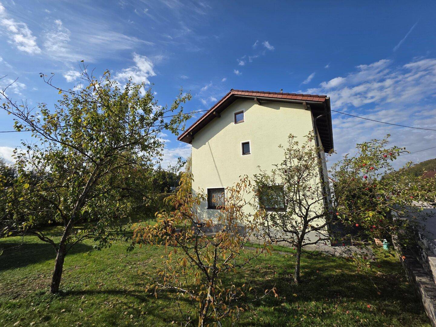 Seitenansicht des Hauses umgeben von Obstbäumen und grünem Rasen unter klarem Himmel.