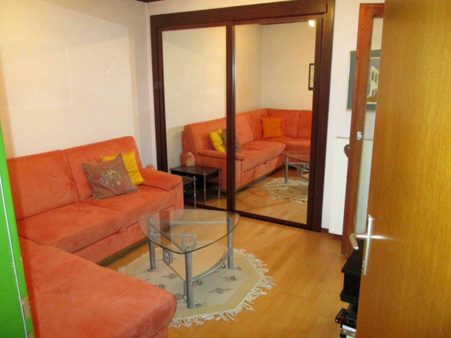 Gemütliches Wohnzimmer mit orangefarbenem Sofa, Spiegelschrank und Parkettboden.