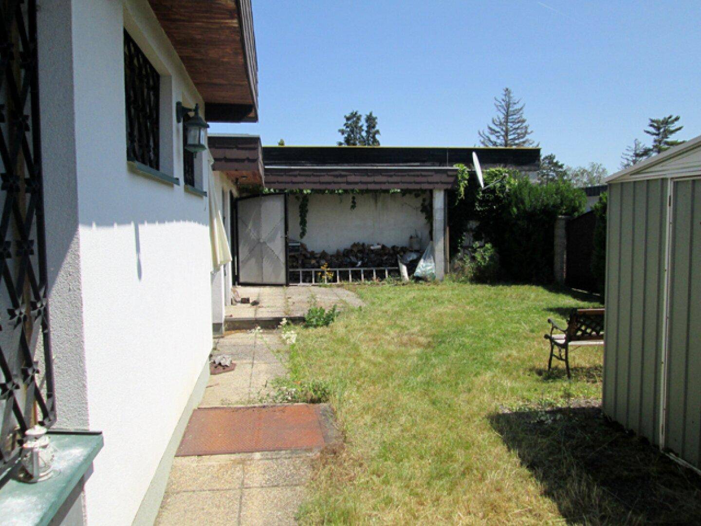 Seitenansicht des Hauses mit Garten, Schuppen und Holzstapel.