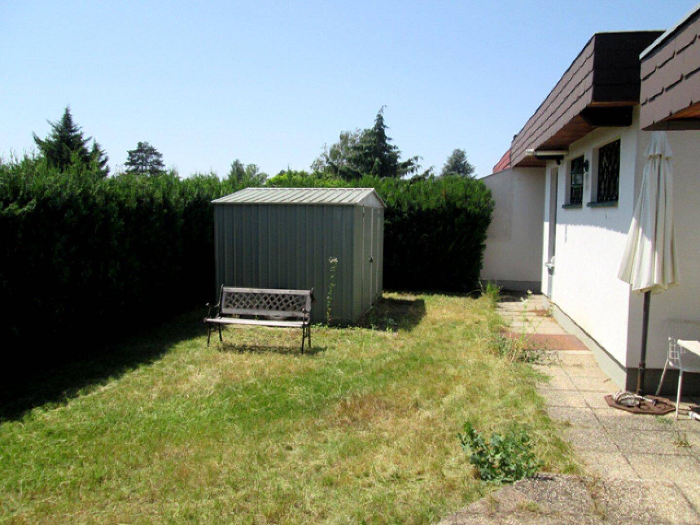 Gartenbereich neben dem Haus mit Schuppen, Bank und Hecke.