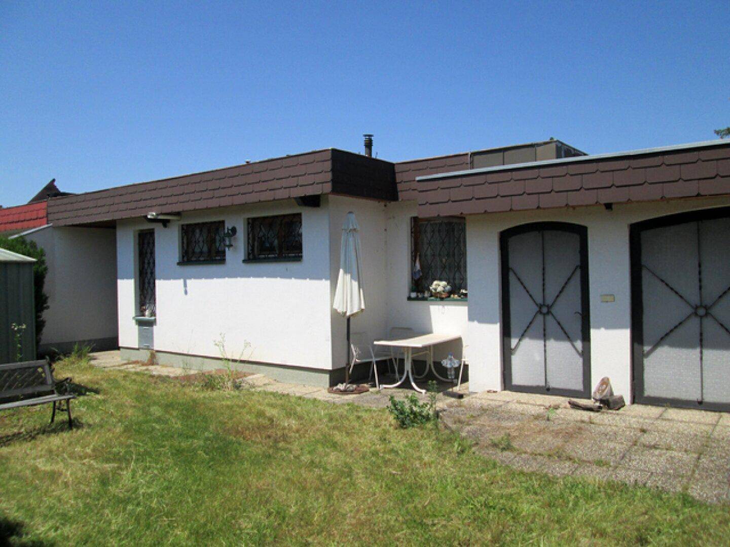 Rückseite des Hauses mit kleiner Terrasse, Gartenbereich und Gartenbank im Sonnenschein.