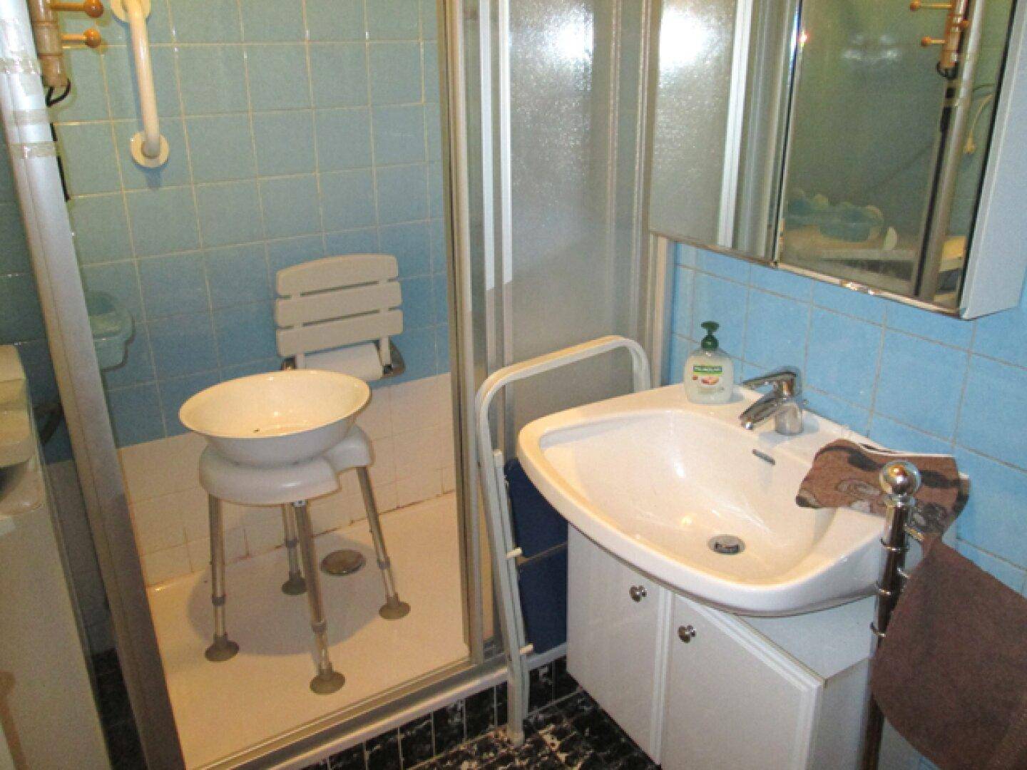 Badezimmer mit hellblauen Fliesen, einer Duschkabine und einem Waschbecken mit Unterschrank.