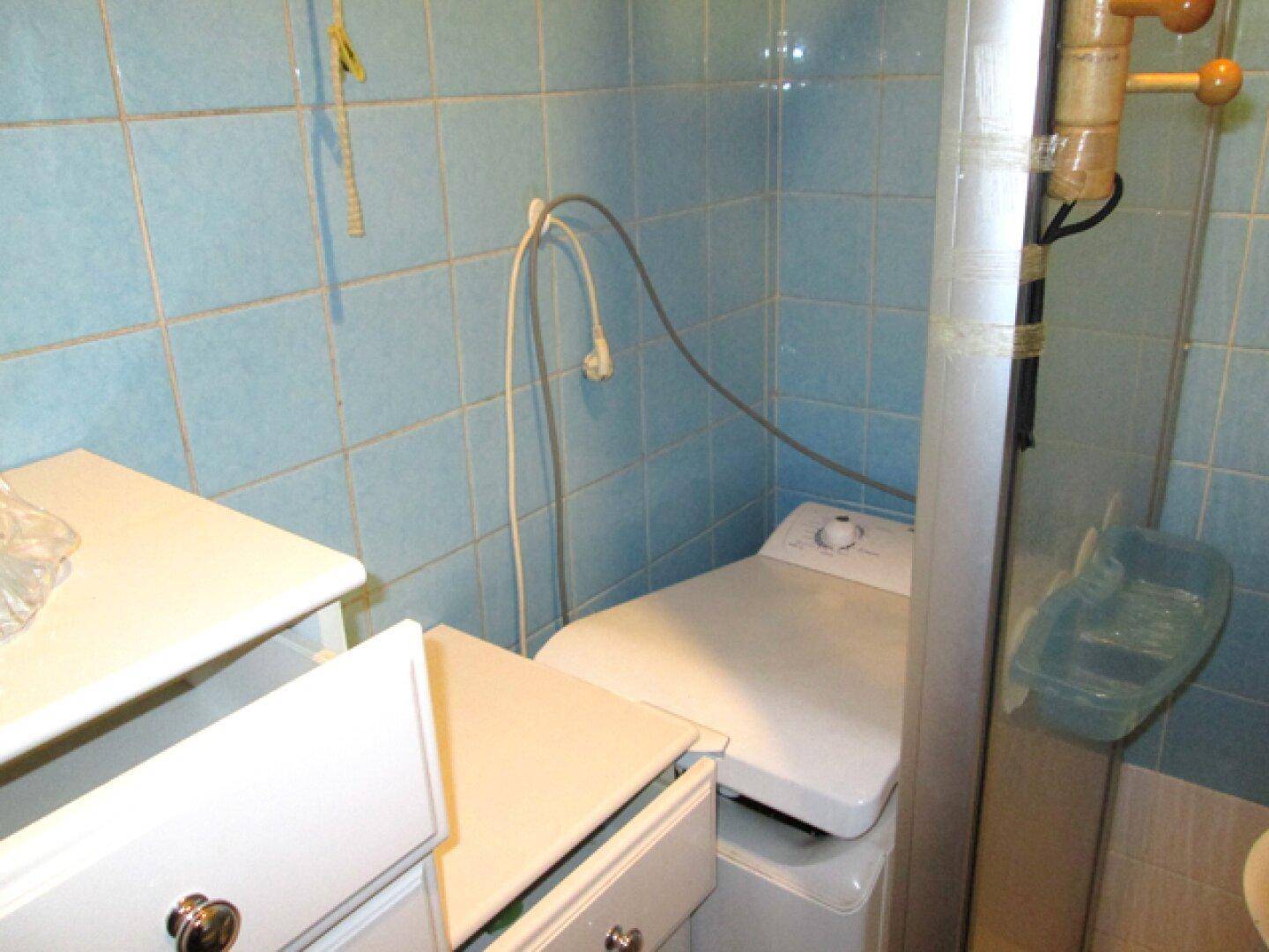 Badezimmer mit blauen Wandfliesen, einer Waschmaschine und einem Duschbereich.