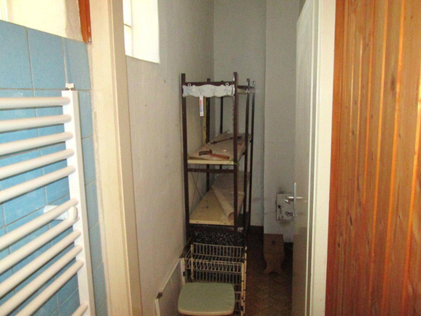 Kleiner Raum mit blauen Fliesen, einem Handtuchheizkörper und einem Regal, möglicherweise ein Abstellraum.