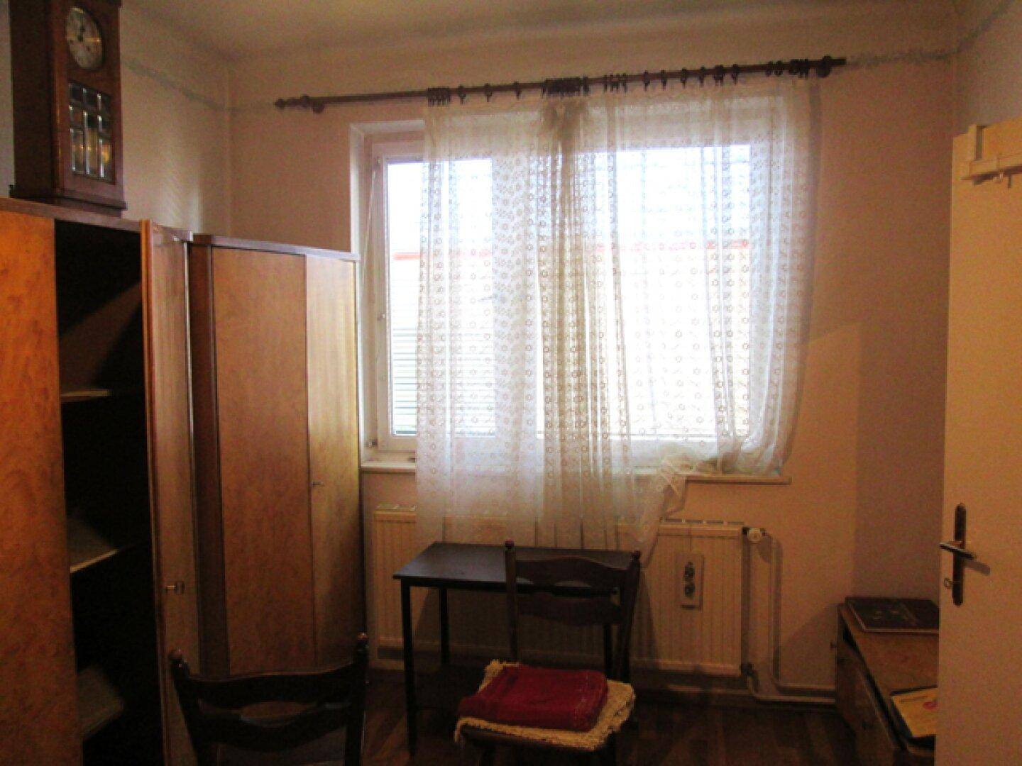 Zimmer mit einem Fenster, einem Kleiderschrank und einem kleinen Tisch.