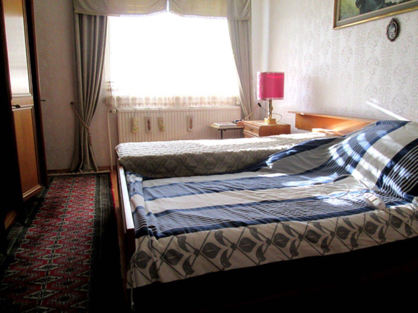 Schlafzimmer mit einem Bett, gemusterter Tapete und einem Fenster mit Vorhängen.