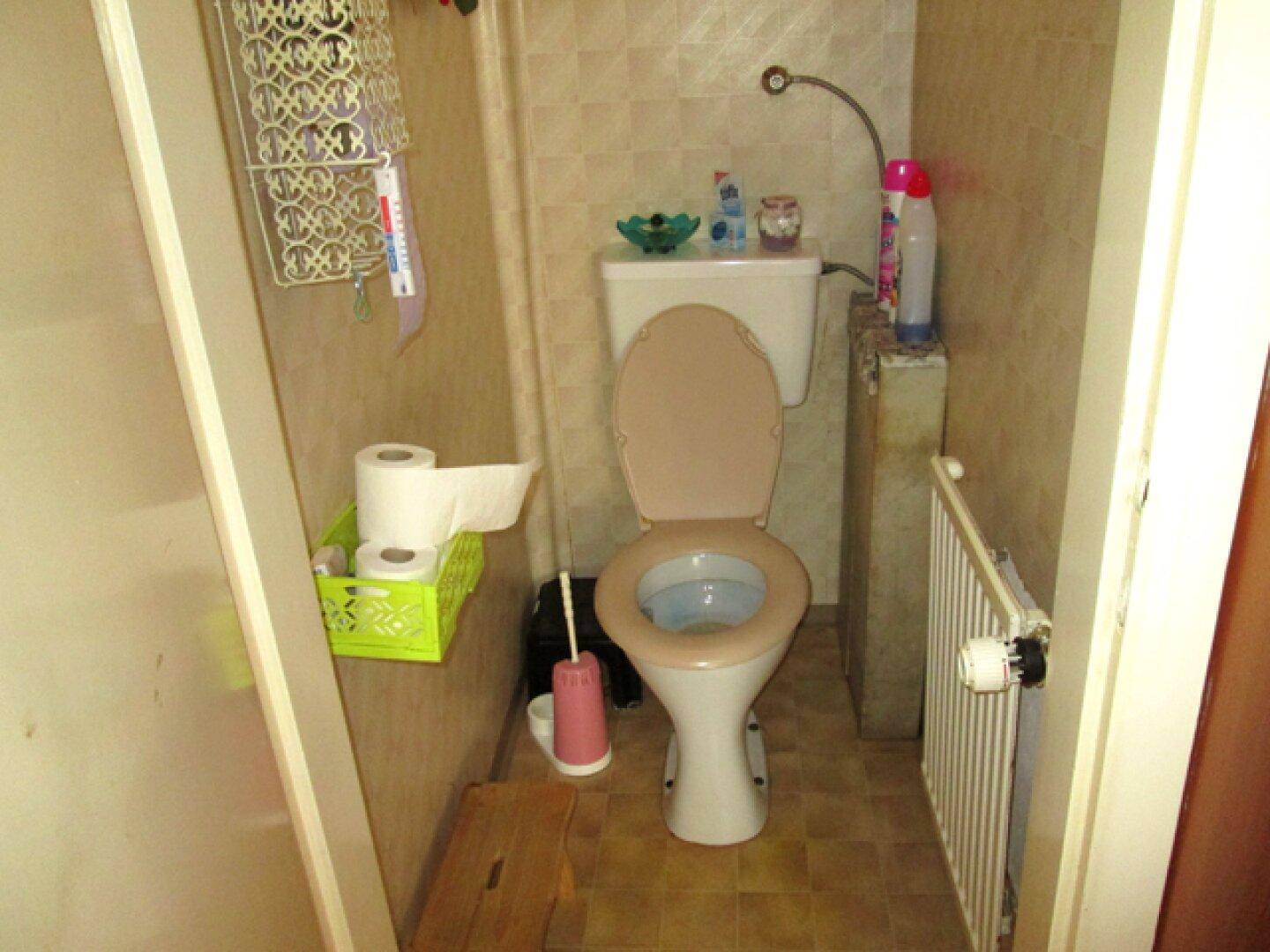 Kleines WC mit Toilette, Fliesenboden und einem Heizkörper.