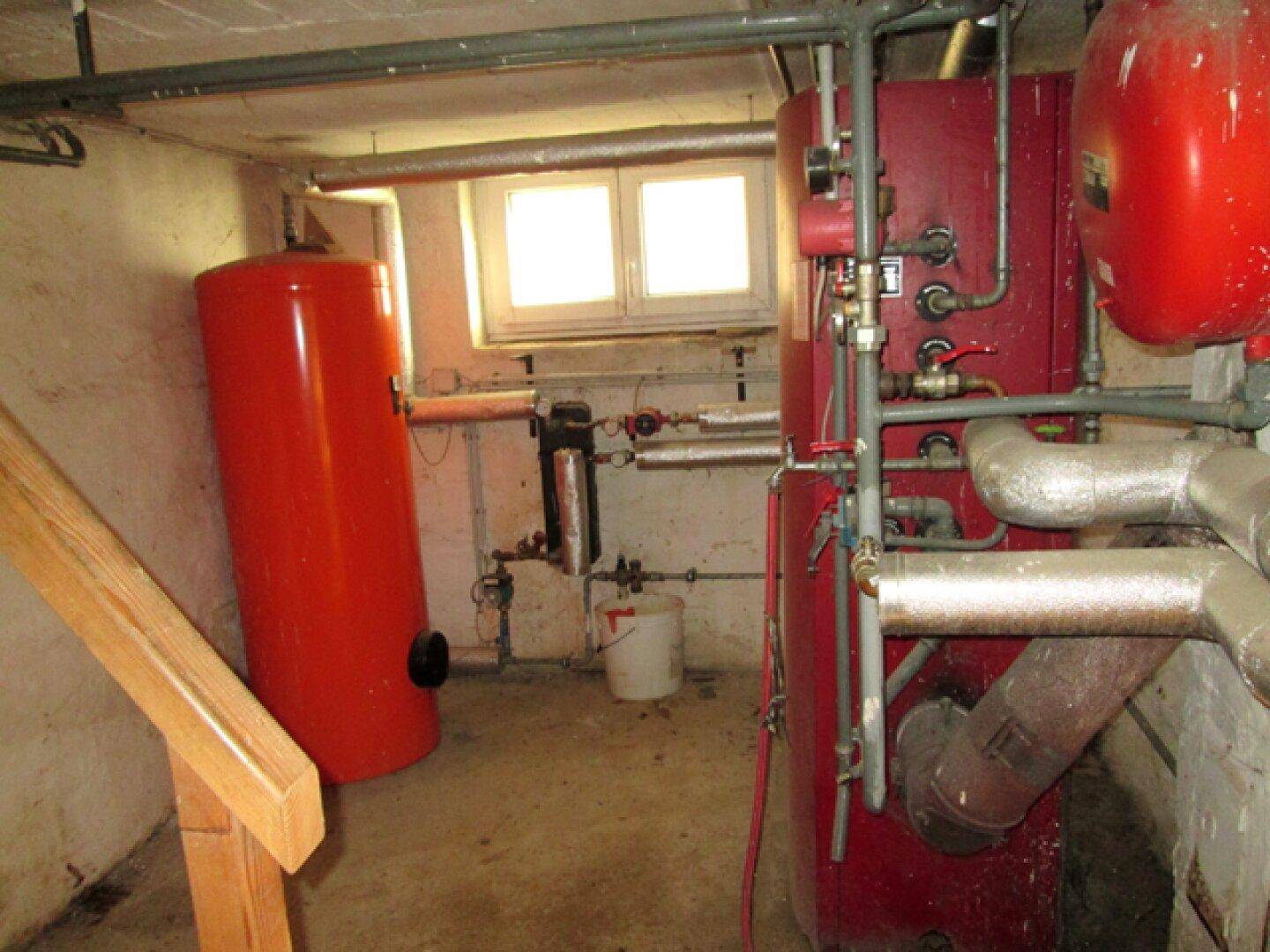 Heizungsraum im Keller mit großen roten Heizkesseln und sichtbaren Rohrleitungen.
