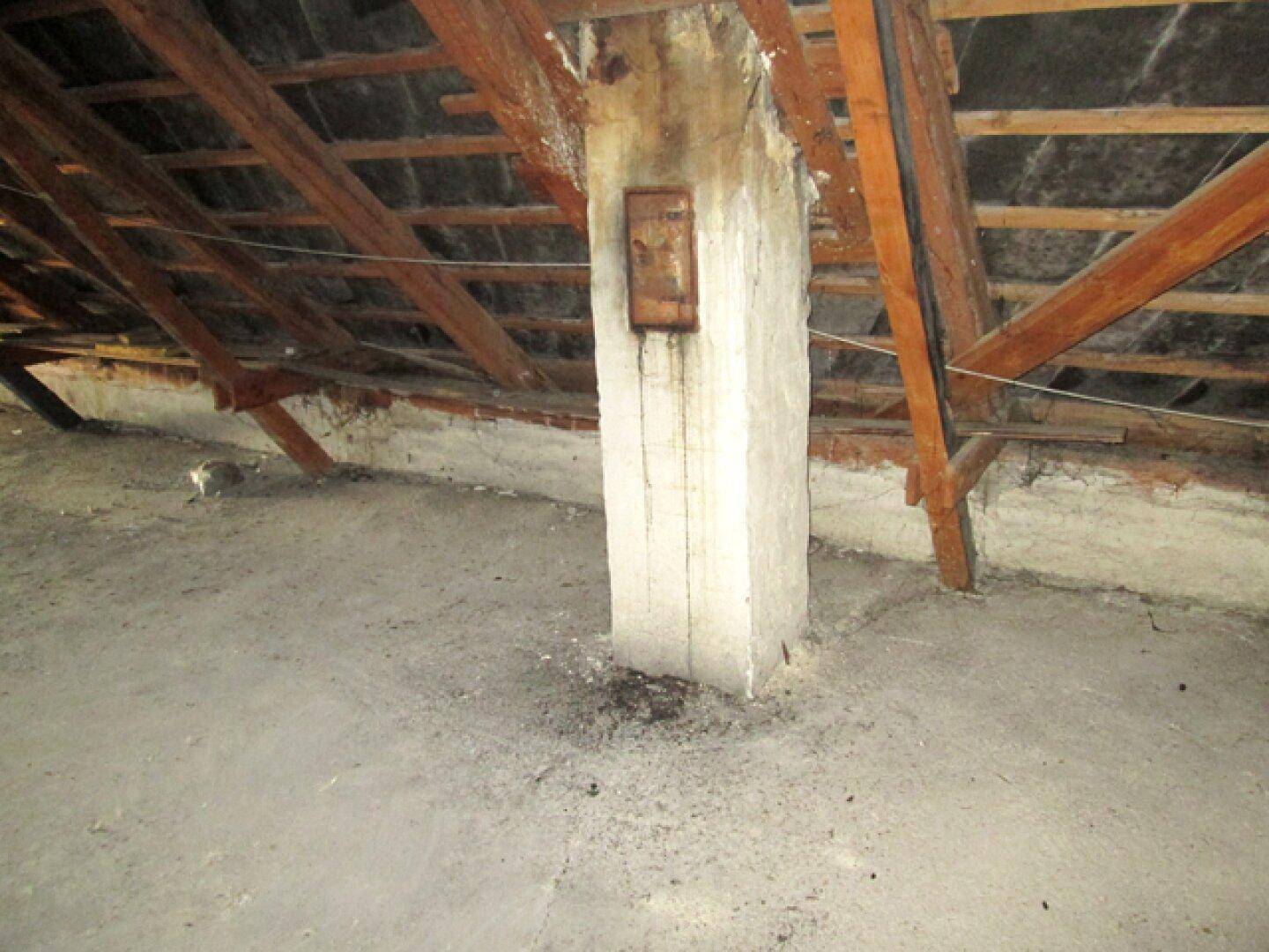 Dachboden mit einem Betonpfeiler, Holzbalken und unfertigem Boden.