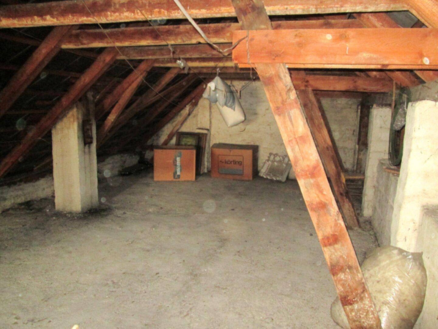 Dachboden mit sichtbaren Holzbalken, schrägen Wänden und ungenutztem Stauraum.