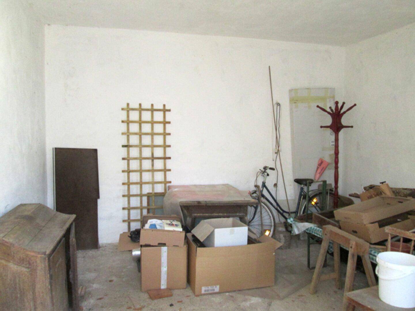 Abstellraum mit verschiedenen Gegenständen, Kartons und einem Fahrrad, der Renovierungsbedarf zeigt.