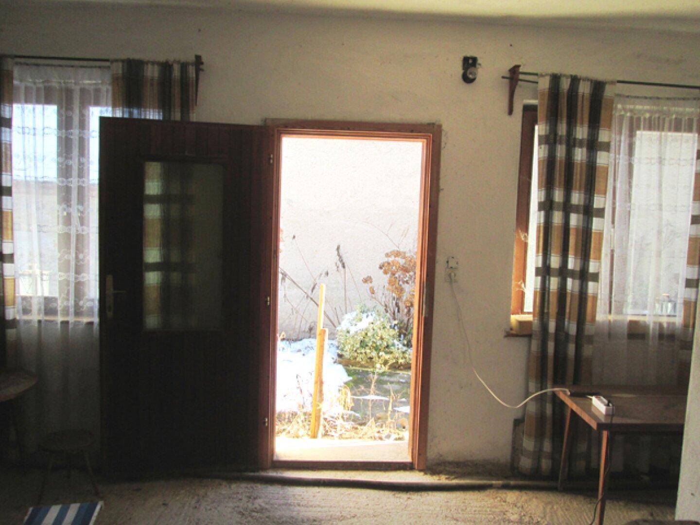 Raum mit offener Tür, die den Blick auf den schneebedeckten Außenbereich freigibt, und Fenstern mit Vorhängen.