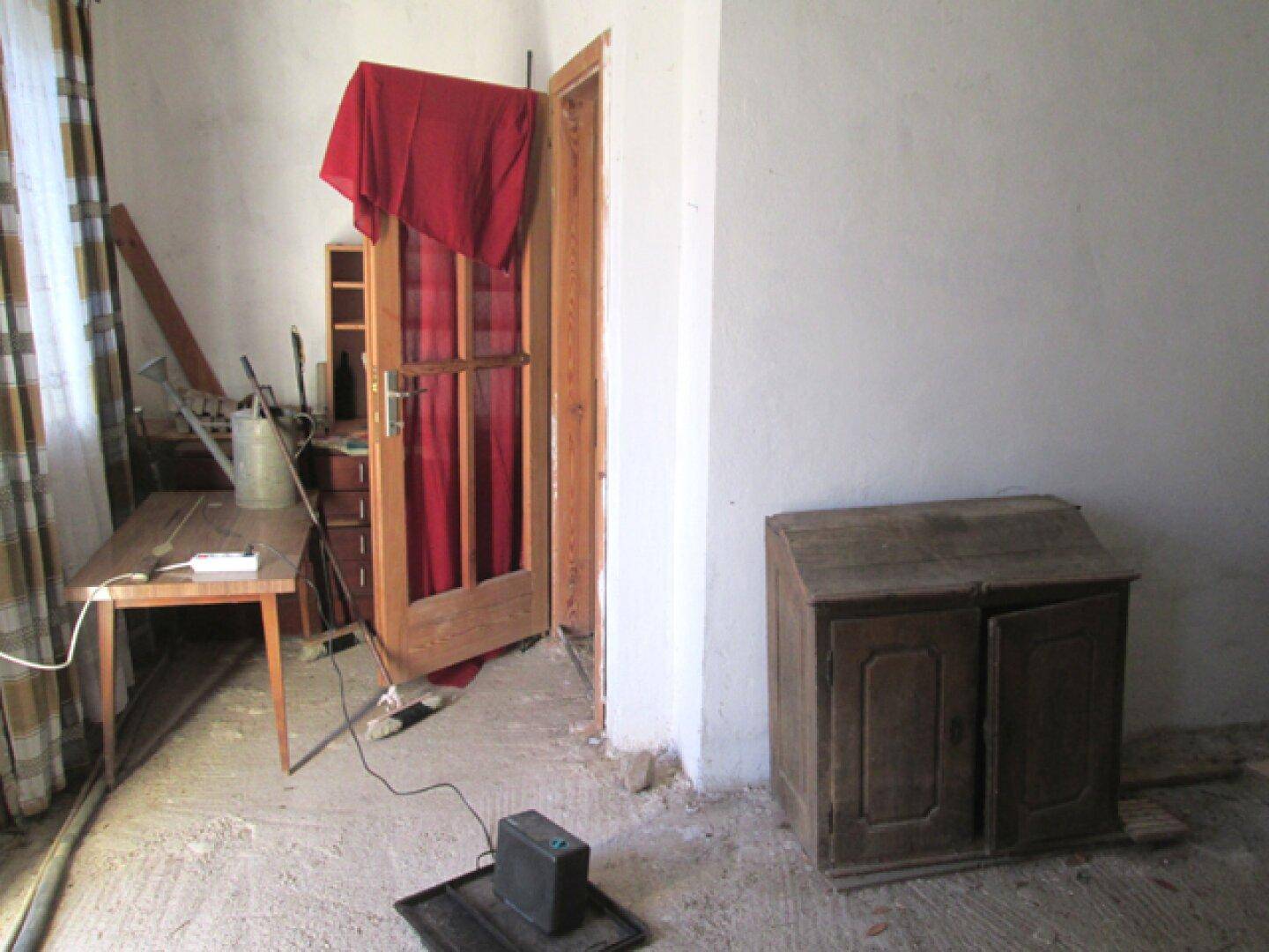 Raum mit einer Holztür, einem Fenster und einem Heizgerät, der Renovierungsbedarf aufweist.