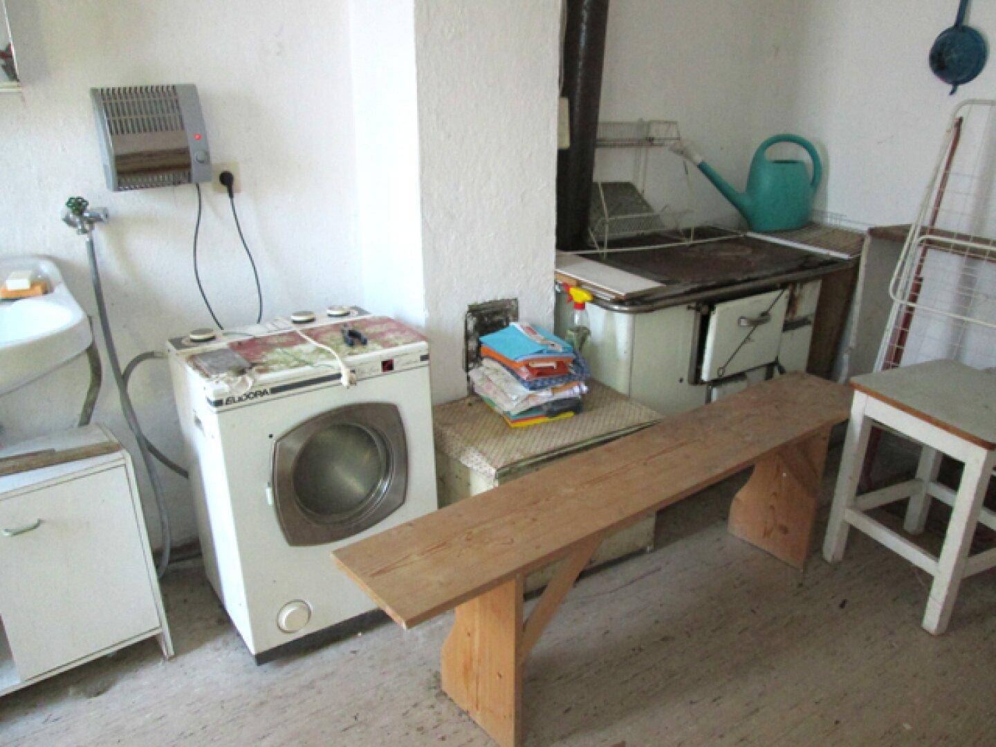 Hauswirtschaftsraum mit einer Waschmaschine, einem Holzofen und einer Holzbank.