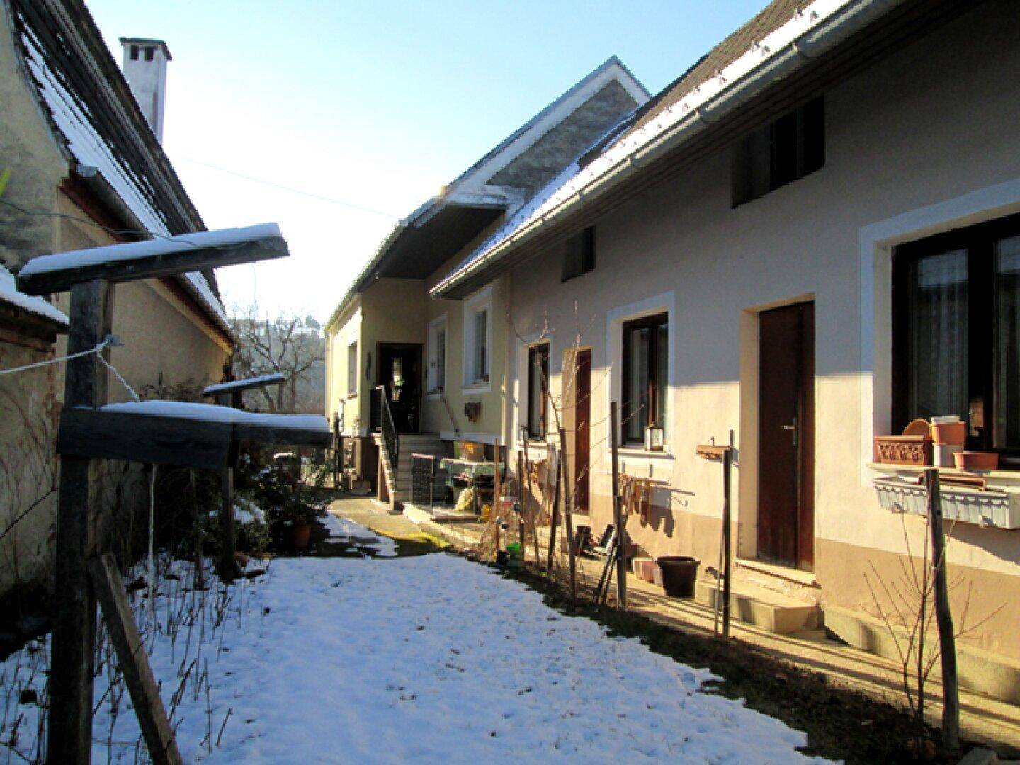 Seitenansicht des Hauses mit schneebedecktem Weg und angrenzenden Gebäuden an einem sonnigen Wintertag.