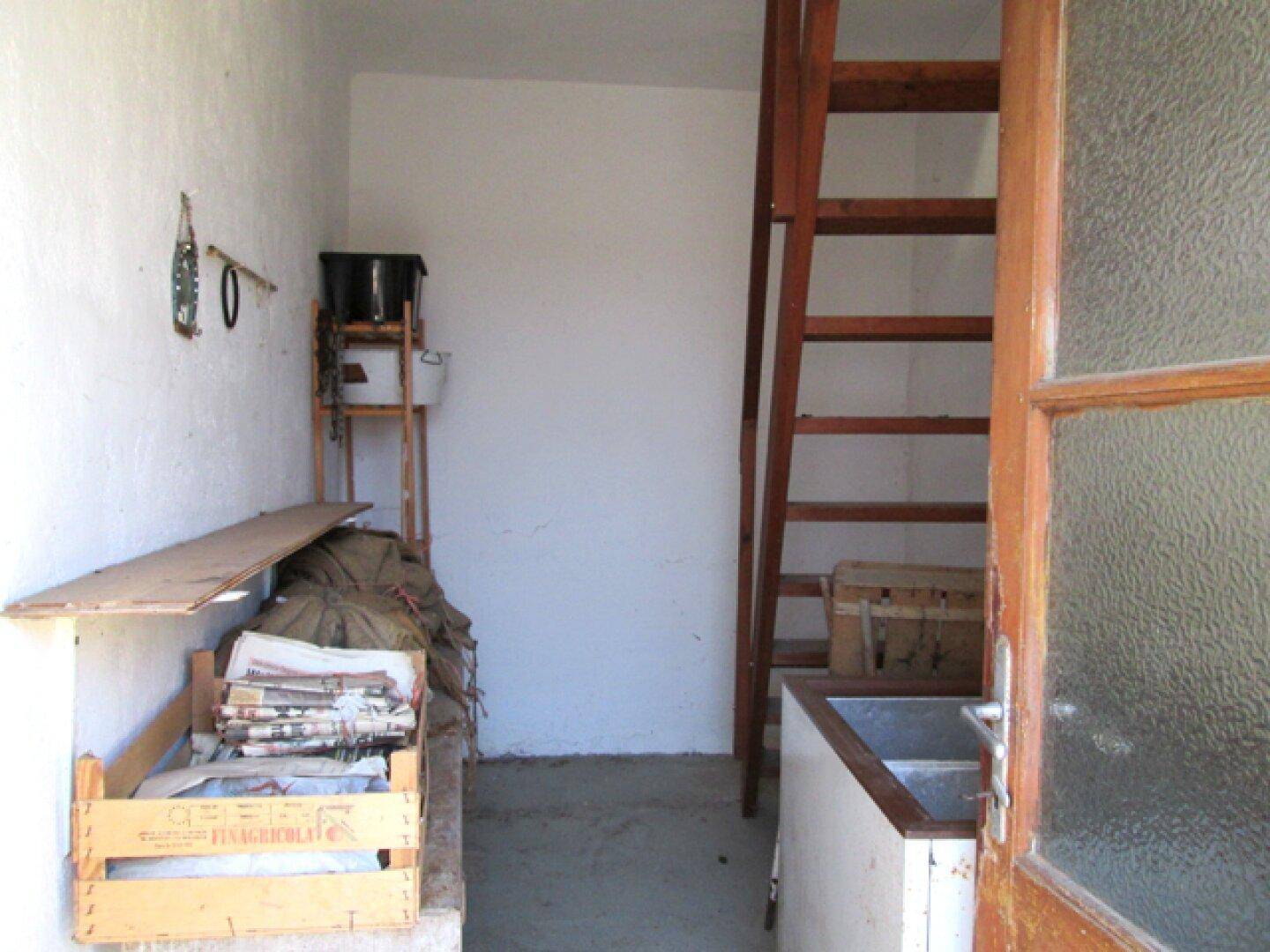 Kleiner Raum mit einer Holzleiter, die zu einem oberen Bereich führt, und gelagerten Gegenständen.