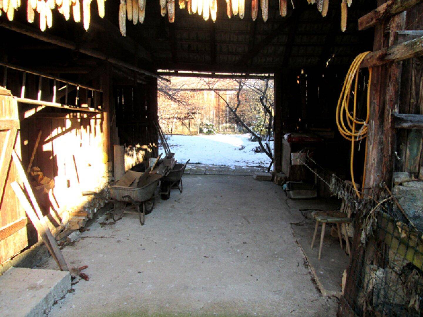 Innenansicht einer Scheune mit Blick auf den schneebedeckten Hof und gelagerten Geräten.