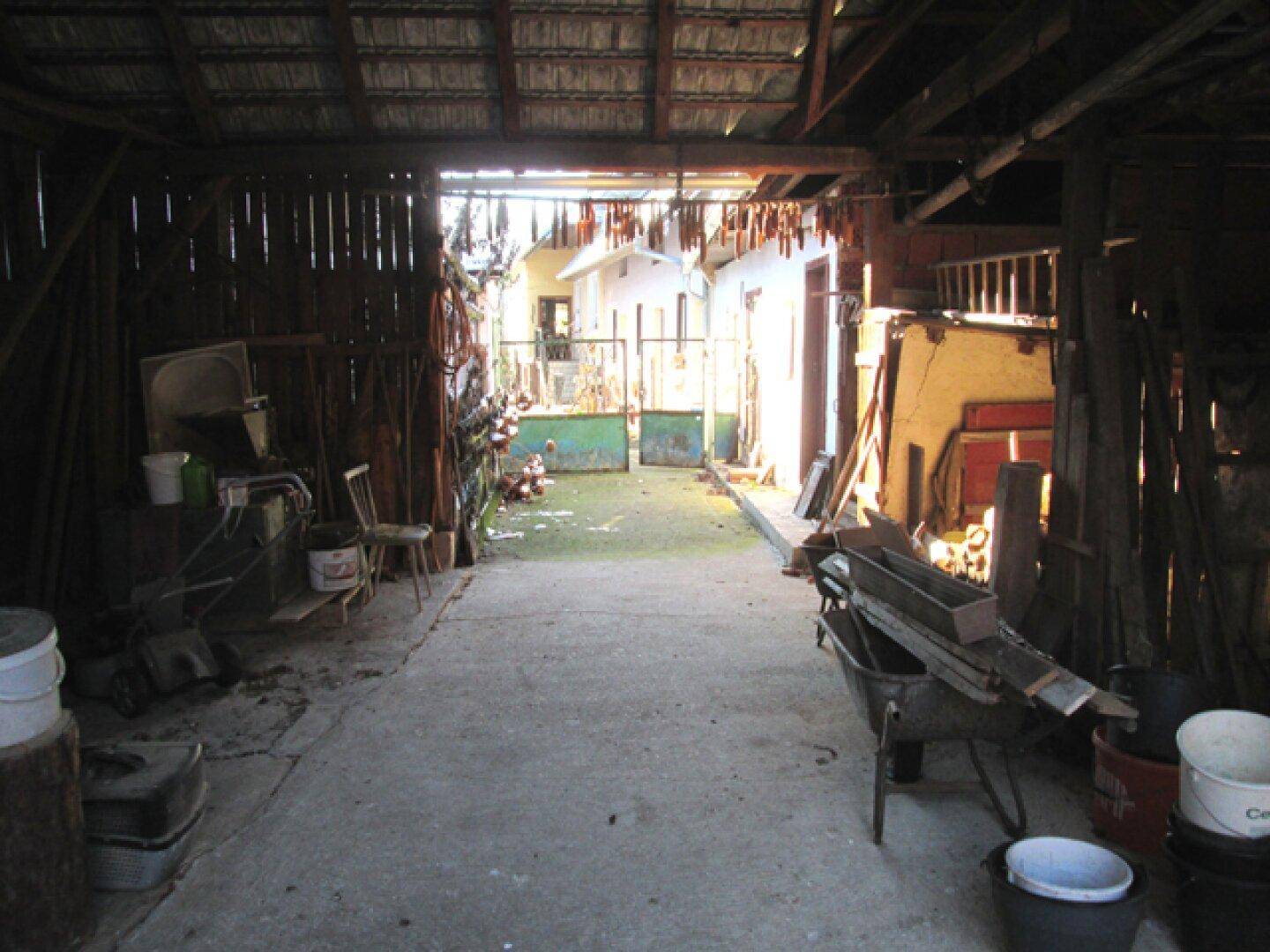 Innenansicht einer Scheune mit Blick auf den Innenhof und gelagerten landwirtschaftlichen Geräten.